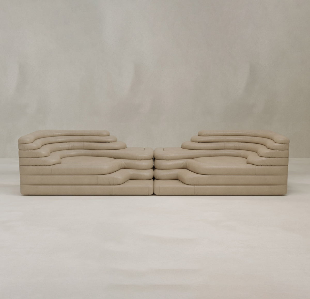 Two Cascata 2 Piece Sofa Rentals, with layered wavy forms and a sculptural beige design, face each other against a light background, adding modern sophistication to any space.
