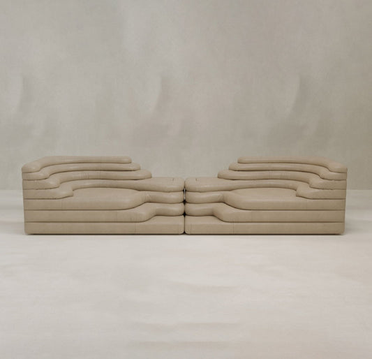Two Cascata 2 Piece Sofa Rentals, with layered wavy forms and a sculptural beige design, face each other against a light background, adding modern sophistication to any space.
