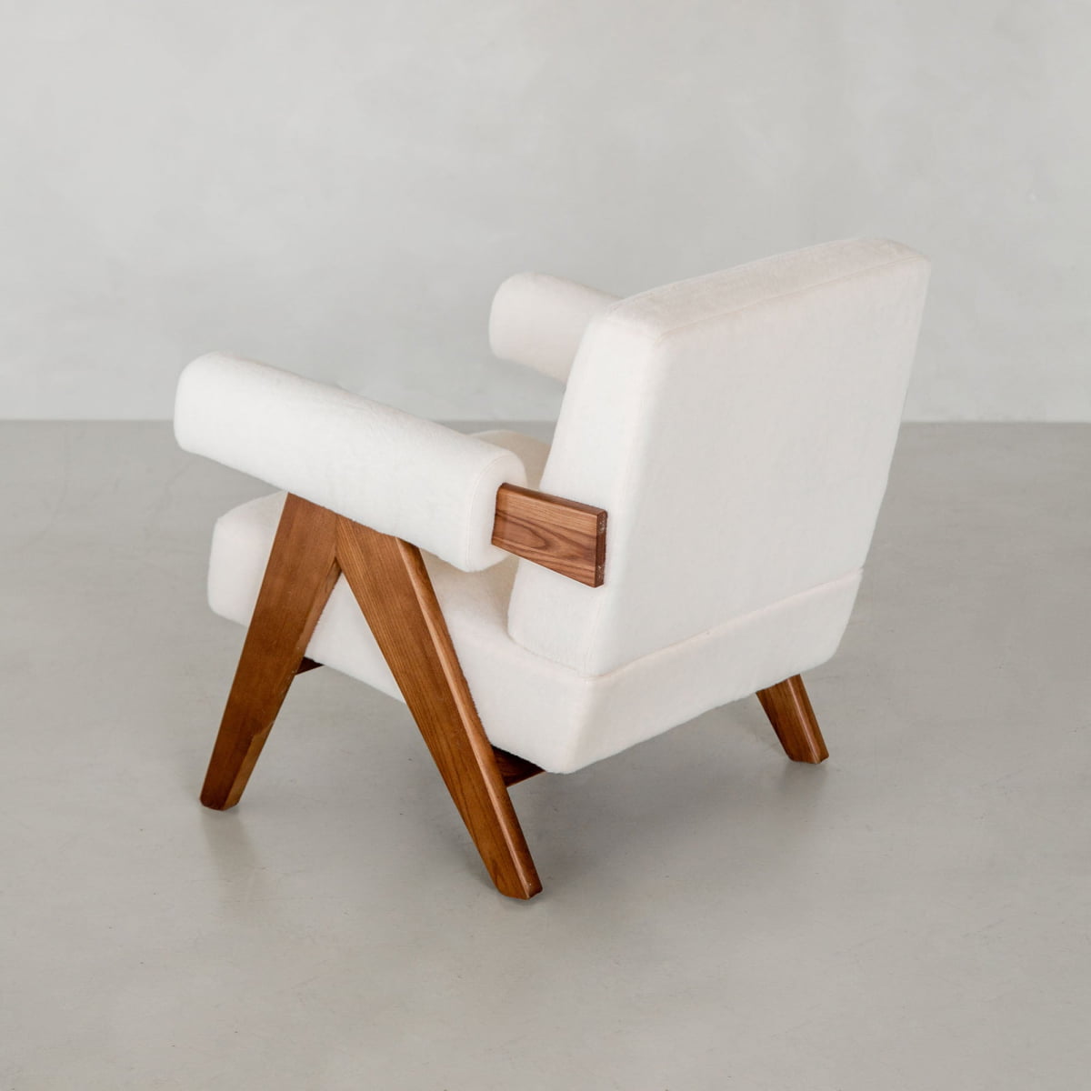 The Chelsea Lounge Chair features white faux mohair upholstery, a wooden frame, and angled wooden legs for a mid-century look, shown on a light floor against a plain light gray wall.