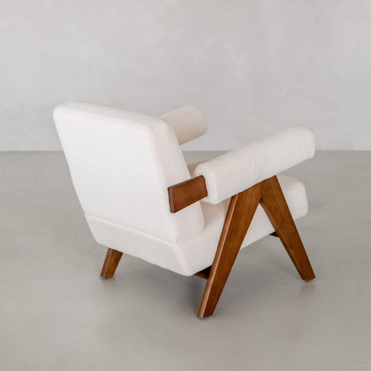 The Chelsea Lounge Chair features white faux mohair upholstery, angled wooden legs, and arm supports. Shown from a back-side view against a light gray background, it highlights its modern mid-century aesthetic.