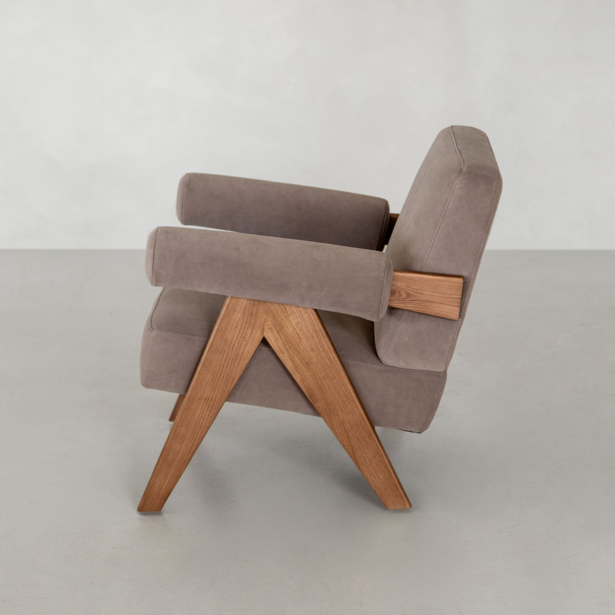 The Chelsea Lounge Chair features taupe faux mohair upholstery and angular wooden legs and arms, shown side-on against a plain light background, offering a refined mid-century style.