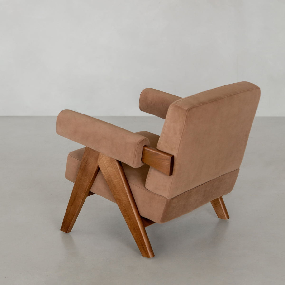 The Chelsea Lounge Chair features light brown faux mohair upholstery and angular wooden legs and arms, shown at an angle on a light gray floor with a pale wall backdrop, showcasing its modern mid-century design.
