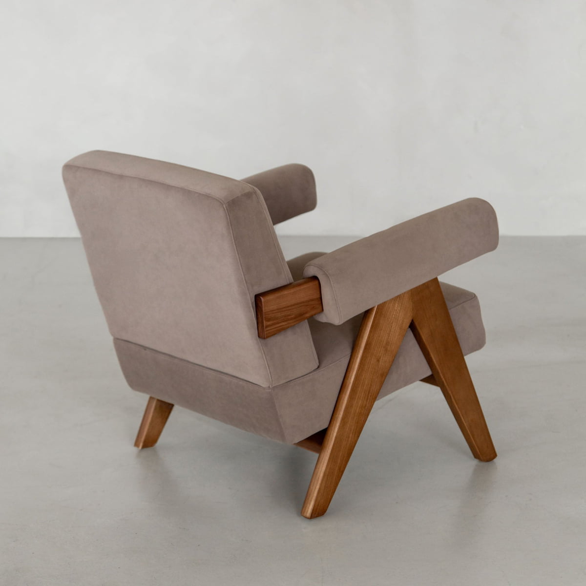 The Chelsea Lounge Chair features light brown faux mohair upholstery and angled wooden legs and armrests, set on a plain light floor against a neutral wall, highlighting its refined mid-century style.