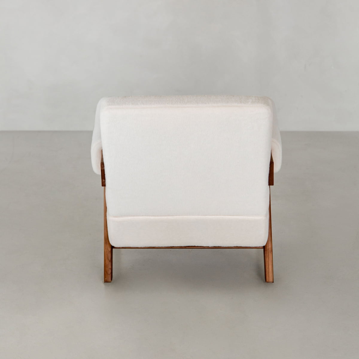 The Chelsea Lounge Chair features soft white faux mohair upholstery and wooden legs, shown from the back against a light gray background, showcasing its chic mid-century modern style.