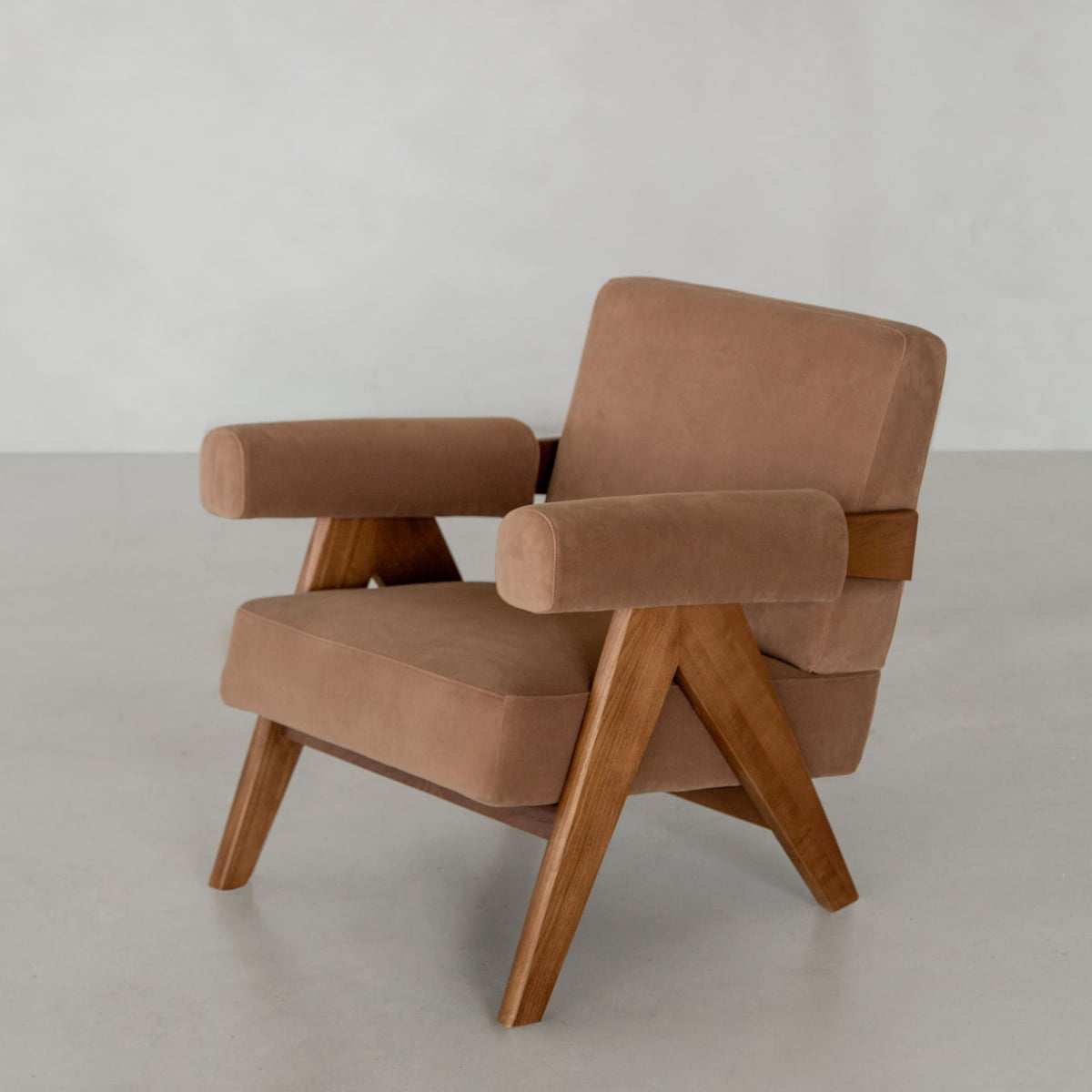 The Chelsea Lounge Chair features a plush, light brown faux mohair seat and backrest, wide armrests, and angled wooden legs, creating a distinct mid-century look on a light gray floor.