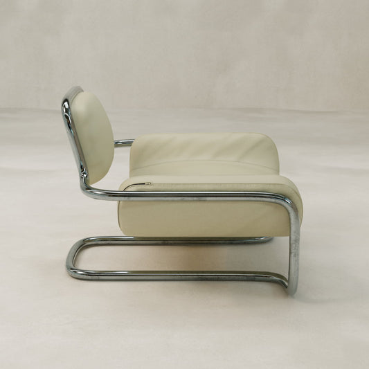 The Citron Chair features a tubular chrome frame and cream cushioned seat and backrest, exemplifying modern aesthetics. Shown in profile against a neutral, textured background.
