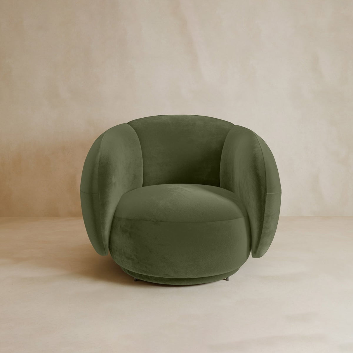 The Clara Armchair, with plush olive green velvet upholstery, rounded arms, and a curved back, sits on a neutral beige floor against a light beige textured wall, adding contemporary style to the space.
