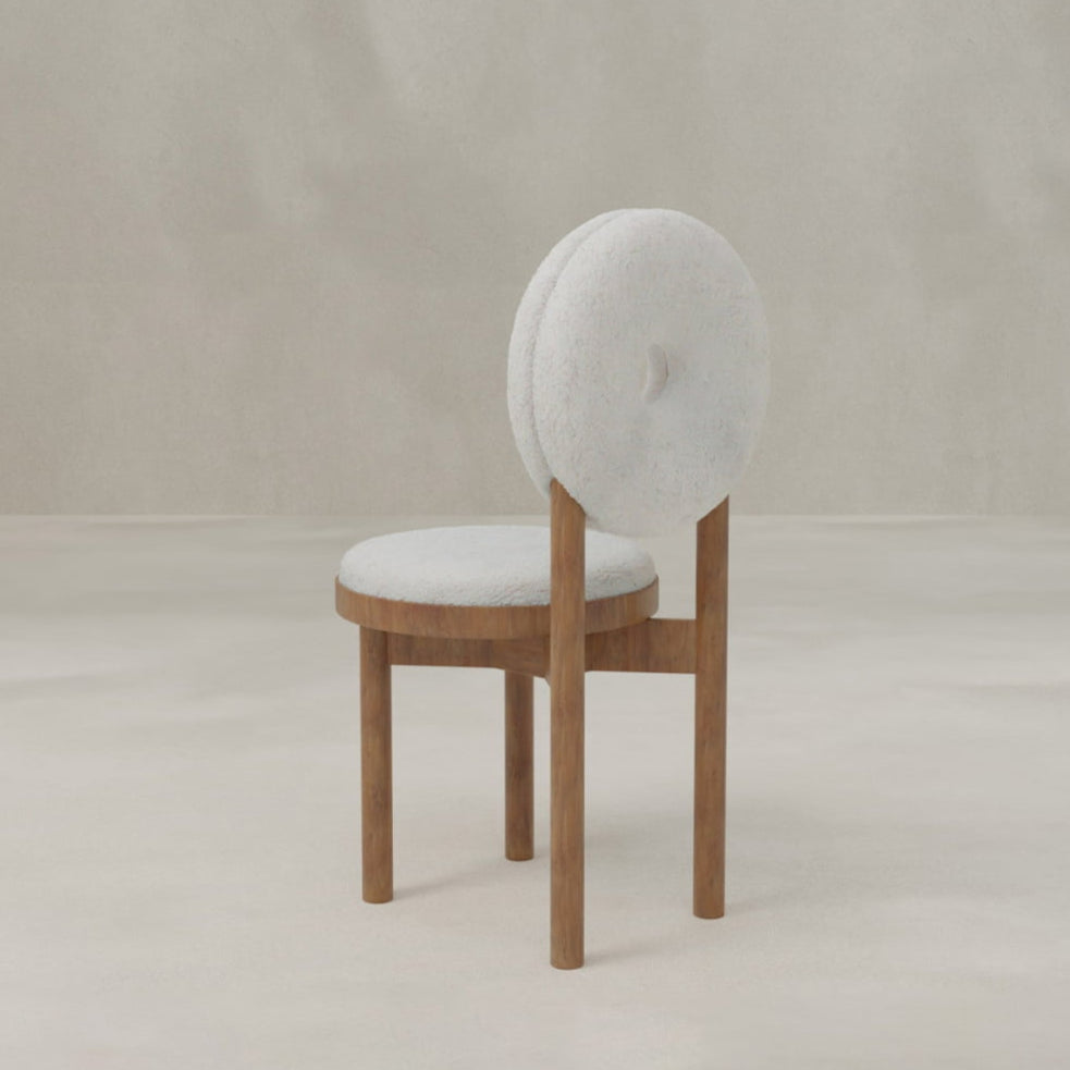 The Donut Chair features a round, cushioned seat and unique seat-back in light fabric upholstery, supported by a wooden frame with three straight legs. Set against a neutral background, it’s the perfect statement piece for any modern space.