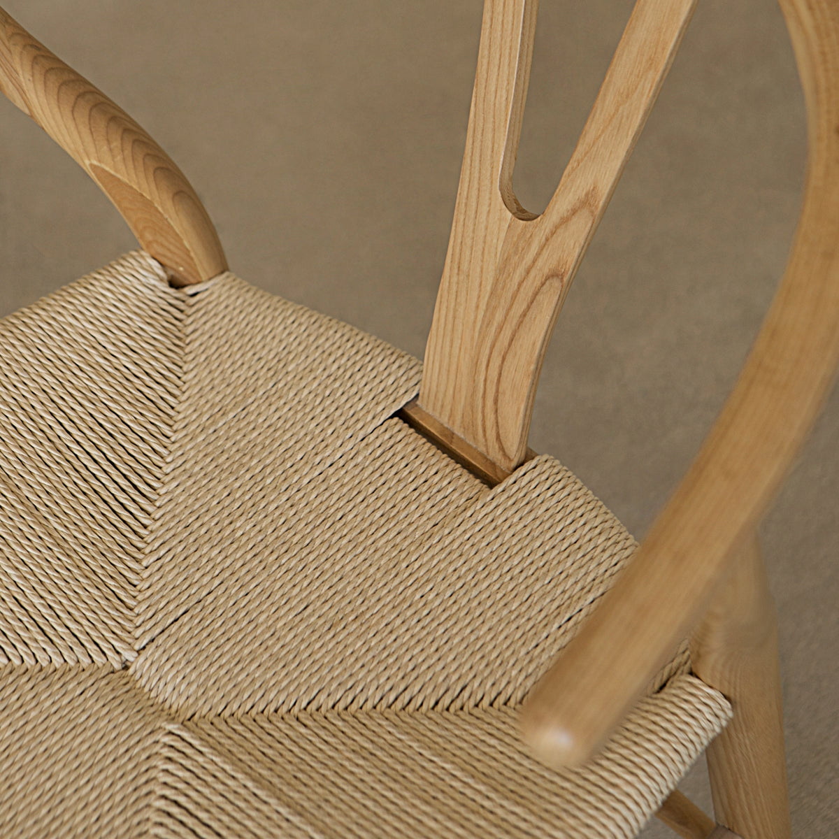 Close-up of the Nola + Elsa Dining Set: a woven seat chair with curved backrest and natural wood grain, highlighting detailed craftsmanship, paired with a round wood dining table against a neutral background.