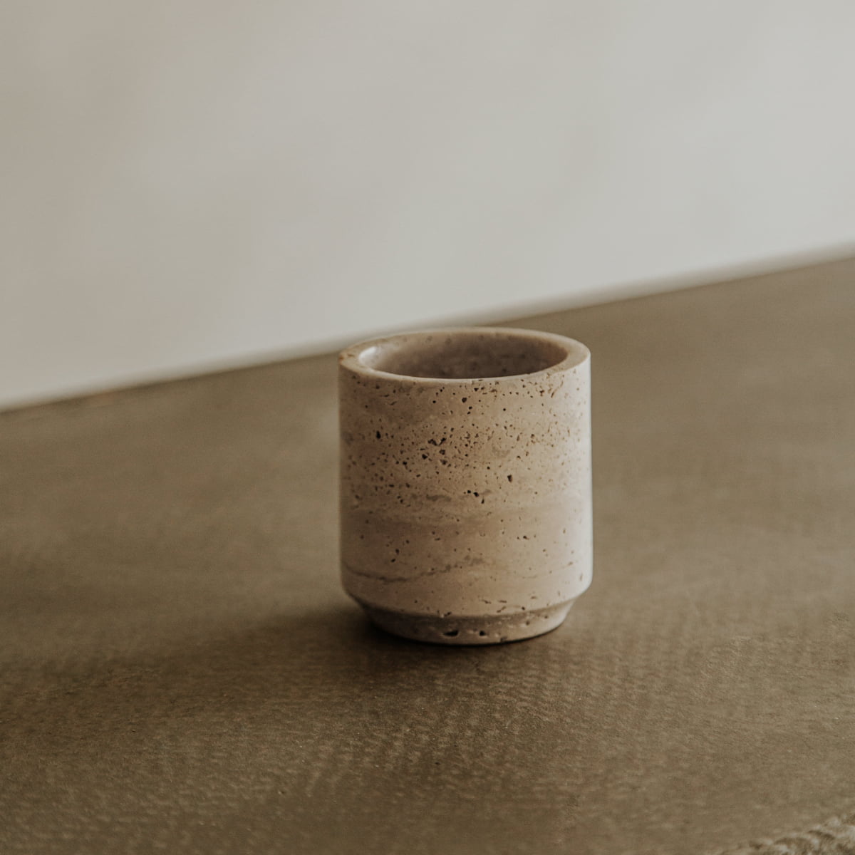 The Étoile Travertine Pen Holder, a small beige ceramic cup with a smooth, speckled finish, exudes subtle French elegance—perfect as a minimalist desk organizer on any textured or plain surface.