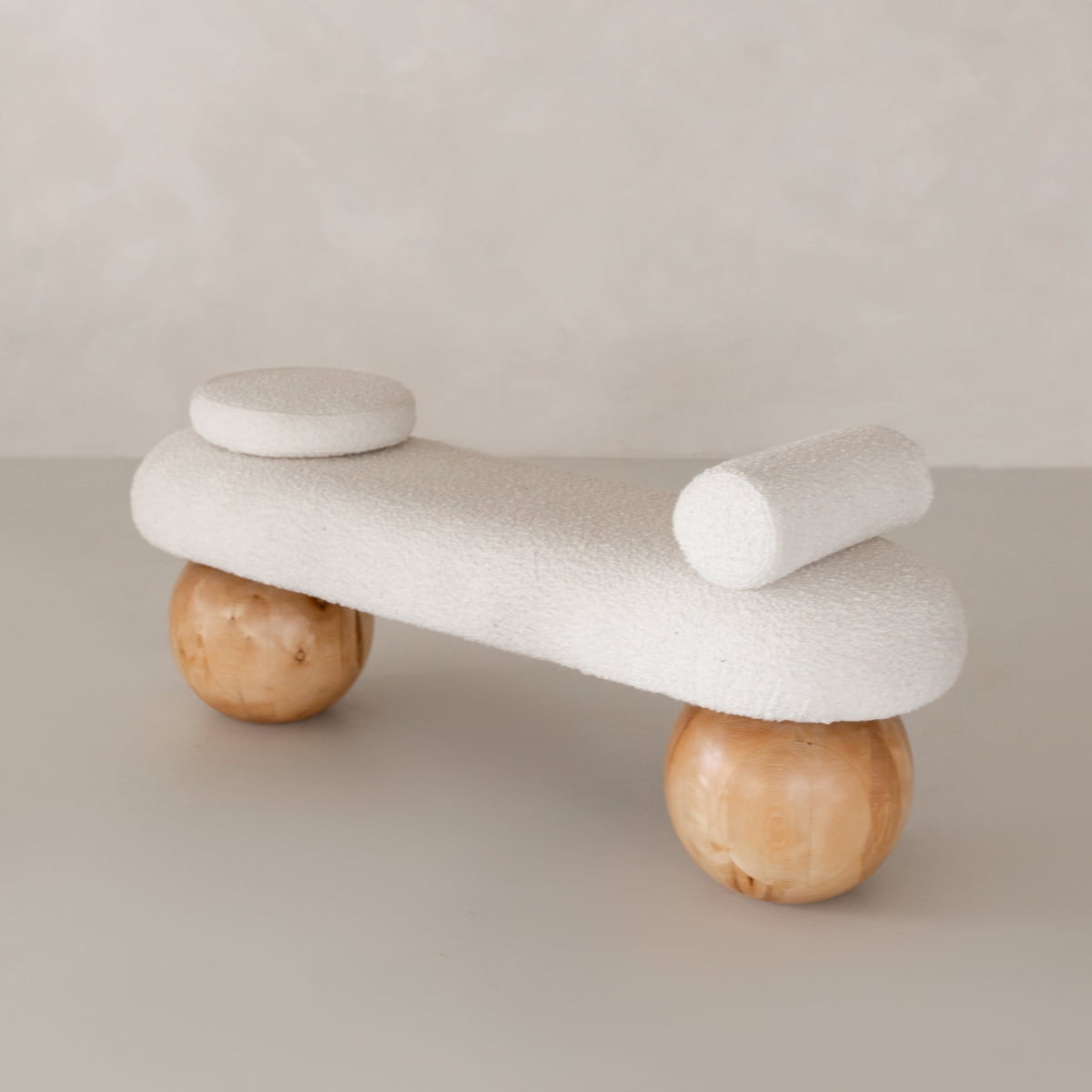 The Finchley Bench features a white textured seat, cylindrical backrest, round cushion, and two large wooden spherical legs—ideal for bringing modern sophistication to contemporary spaces.