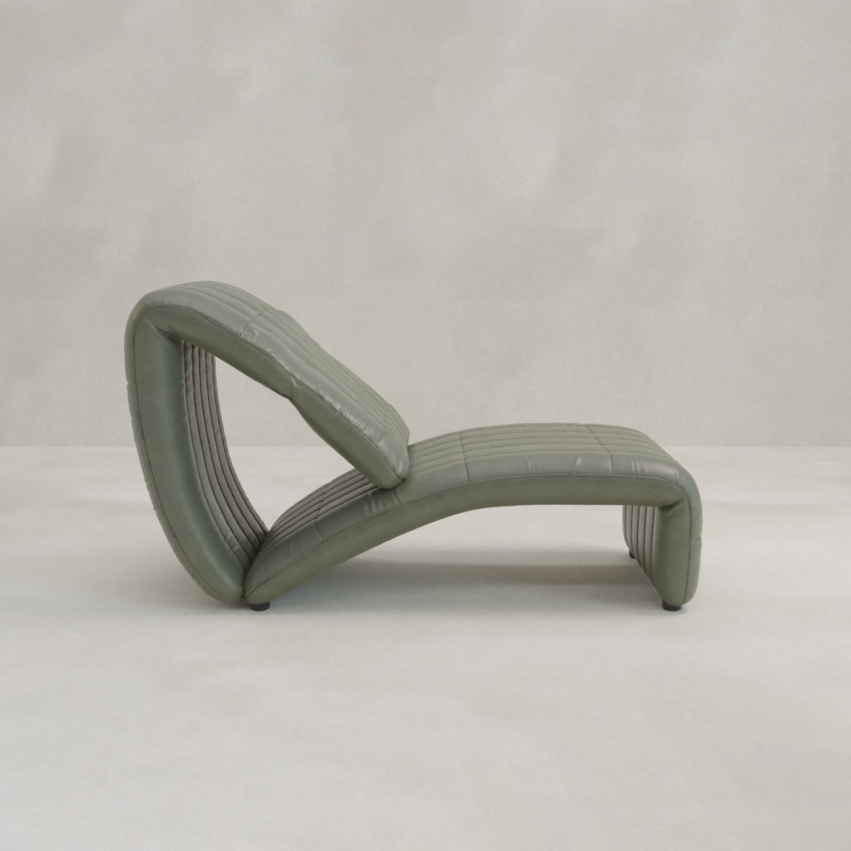 The Hillier Chair is a modern, sculptural chaise lounge with smooth green upholstery and a curved, continuous design featuring subtle reclining elements, set against a plain light gray background.
