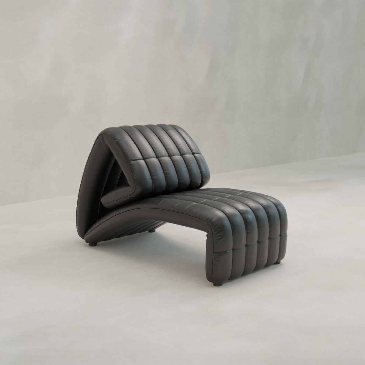 A modern, black Hillier Chair with reclining features and a ribbed, cushioned surface in premium vintage leather sits on a light floor against a neutral wall.