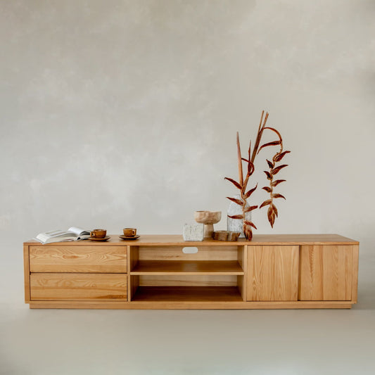 The Indre Media Console features drawers and shelves for ample storage, styled with dried plants in a vase, stacked wooden bowls, cups, and an open book, all against a neutral backdrop for a modern touch.