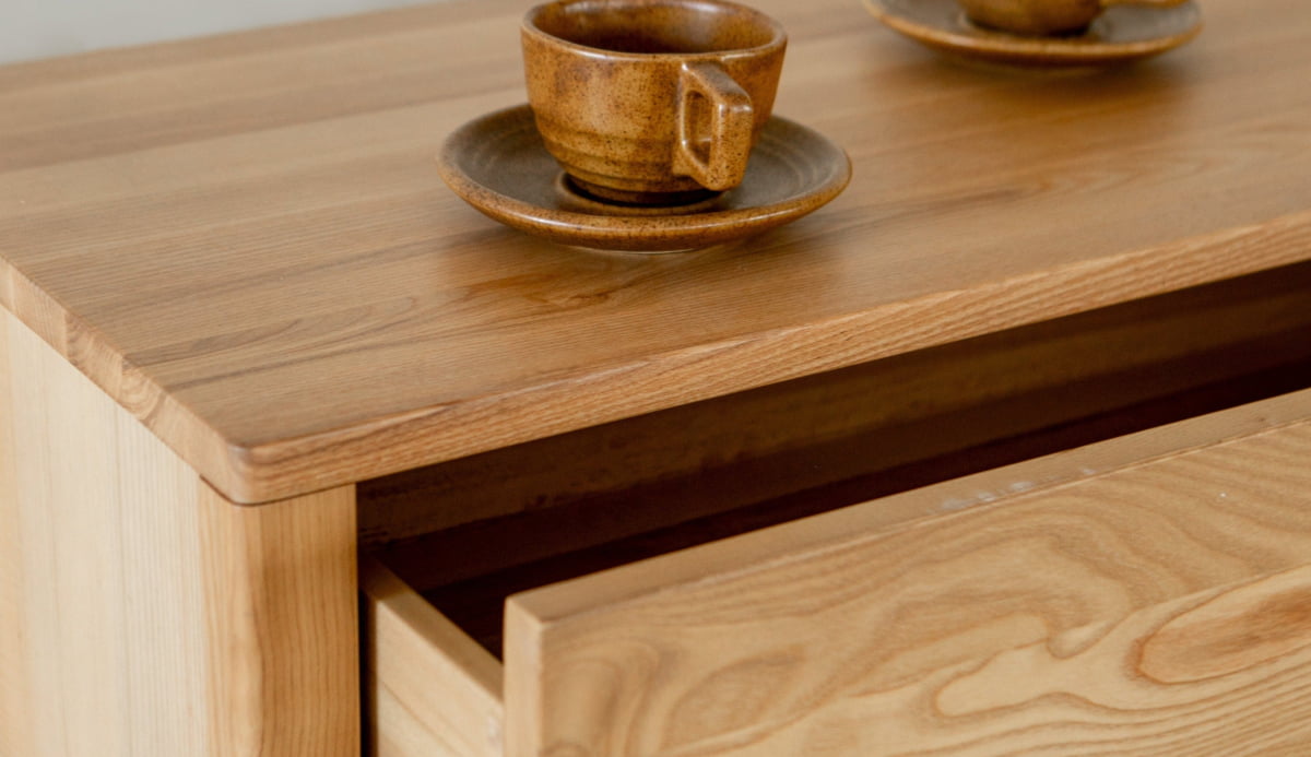 A close-up of the Indre Media Console in light wood with ample storage, one drawer slightly open. On top, two brown ceramic cups with matching saucers enhance the scenes warm, minimalist look.