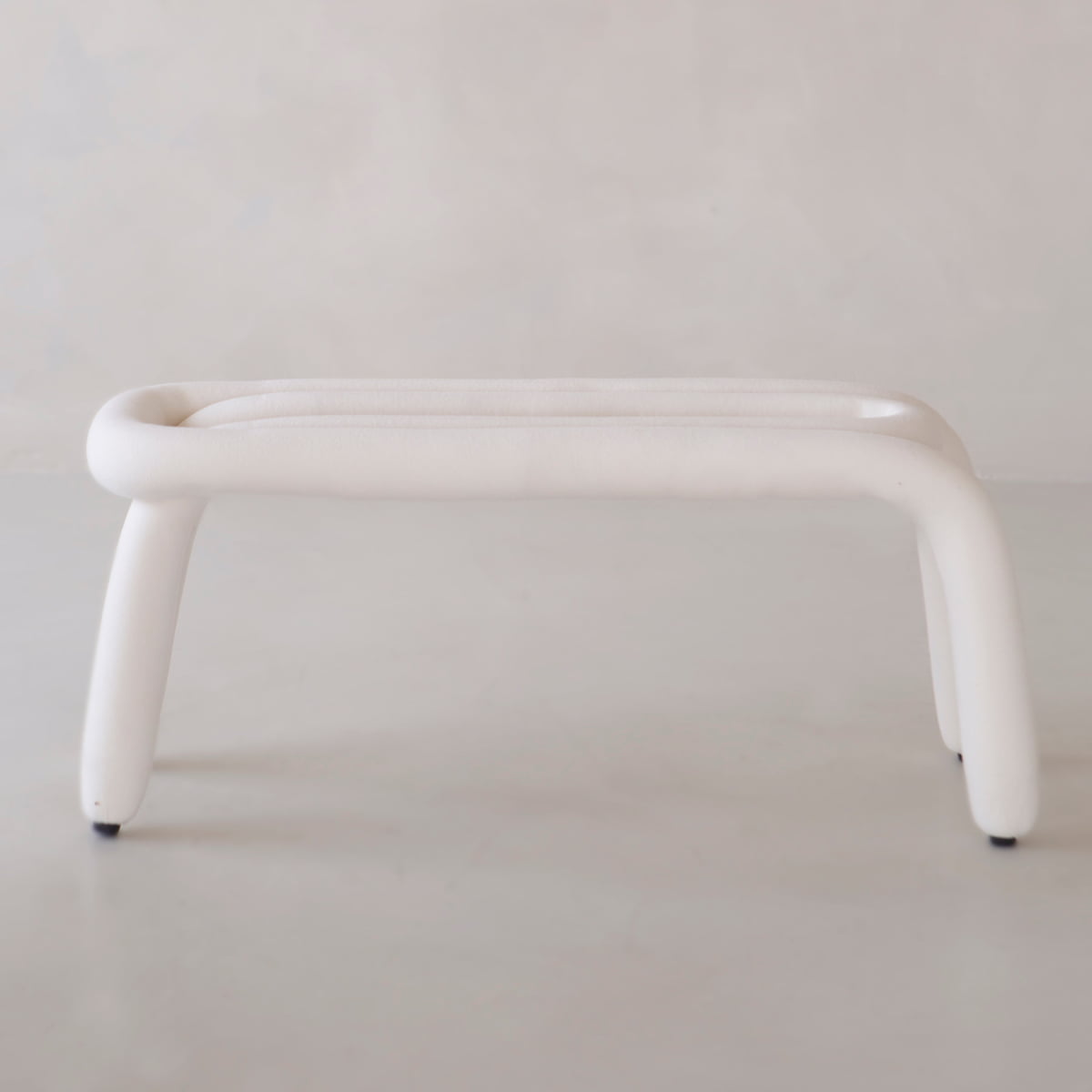 The Loud Bench is a modern, minimalist white bench with four legs and rounded edges, crafted from polyurethane foam and shown against a plain light background.