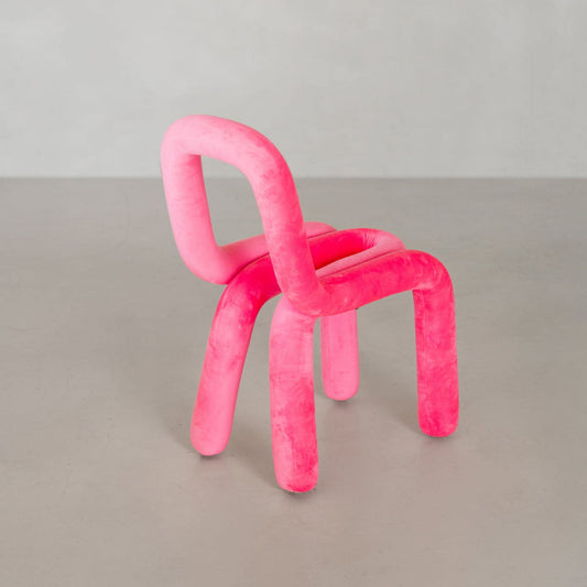 The Loud Chair features thick, tubular, plush pink polyurethane foam shaped into soft curves and angles, showcasing modern design against a plain gray background.