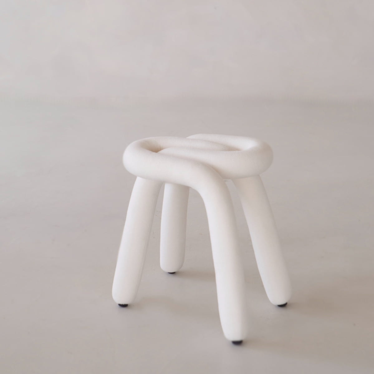 The Loud Stool is a small, modern seat with four chunky, curved legs and a soft tubular polyurethane foam frame, all upholstered in white fabric and shown against a plain light background.
