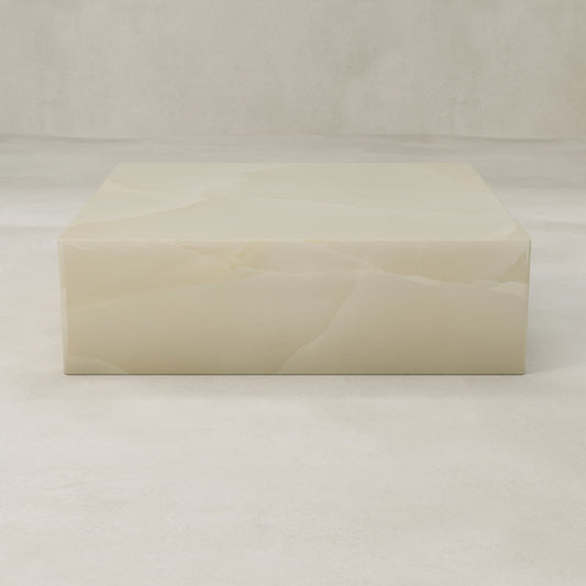 The Lunelle Onyx Coffee Table XL is a square, cream-hued piece with a polished surface and delicate golden veining, set in a minimal, light-toned room featuring matching floors and background.