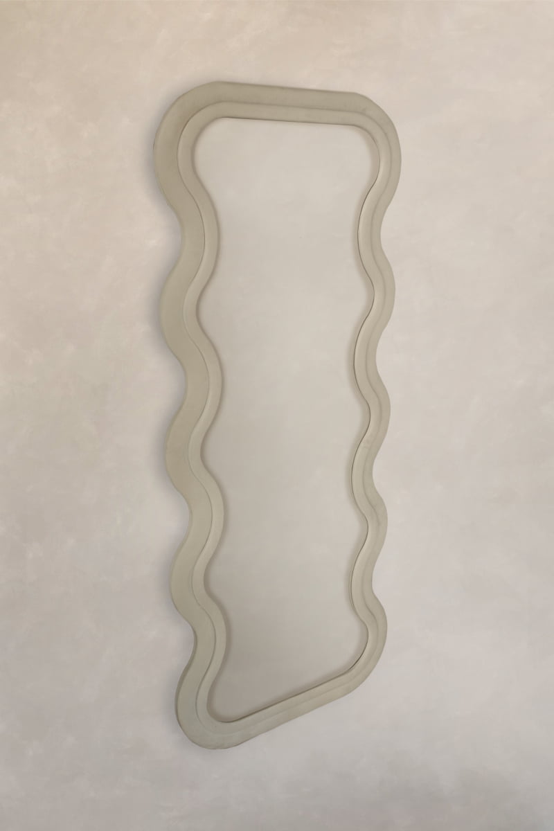 The Onde Mirror Large features a thick, wavy velvet frame and is displayed on a light beige textured wall, bringing contemporary sophistication to any space.