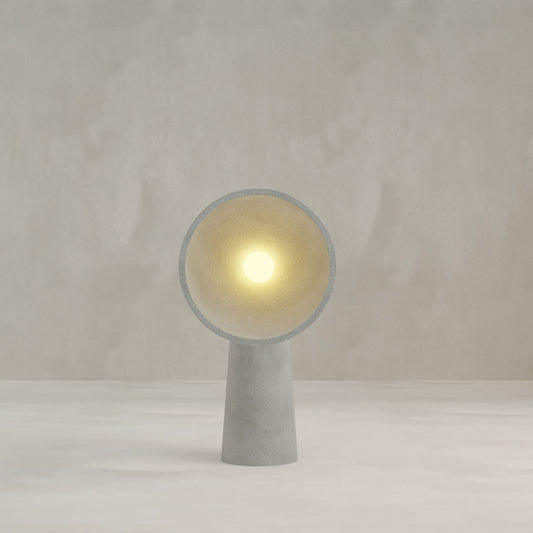 The Orbis Medium Floor Lamp features a minimalist concrete design with a cone-shaped base and circular shade, casting a soft glow against a light background—a sophisticated tribute to sculptural artistry.