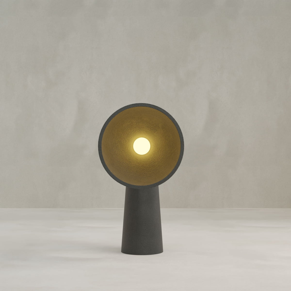 The Orbis Medium Floor Lamp features a modern, minimalist black design with a conical base and wide circular shade. Its gold interior reflects warm light, creating a sculptural look against a plain light gray background.