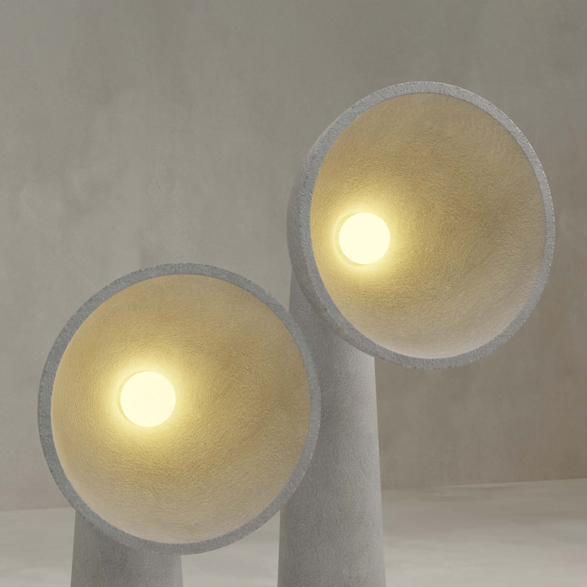 The Orbis Medium Floor Lamp features a minimalist design with a natural stone look. Its sculptural, cone-shaped form and glowing circular bulb create a strikingly modern accent against any neutral, textured backdrop.