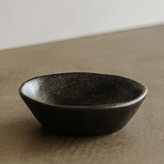 The Pebble Speckled Bowl Large, a spacious black ceramic bowl with a matte finish, rests on a taupe surface against a neutral background.