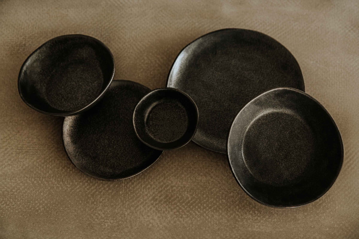 A large Pebble Speckled Bowl is arranged on a textured beige surface, creating a minimalist and modern composition.