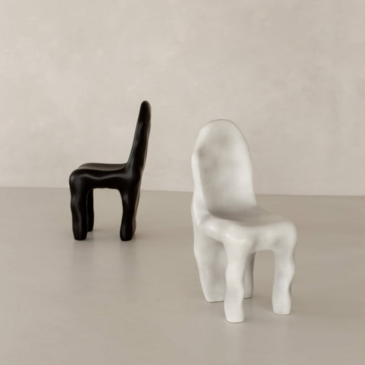 Two Phantom Chair Rentals—one black, one white—with abstract, rounded forms exemplify modern design as they sit on a smooth light-colored floor against a pale minimalist wall.