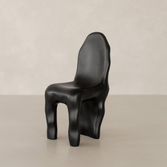 The Phantom Chair Rental features a black, sculptural design with an irregular, organic shape and smoothly contoured legs, showcased against a plain light beige background—a true ode to modern craftsmanship.
