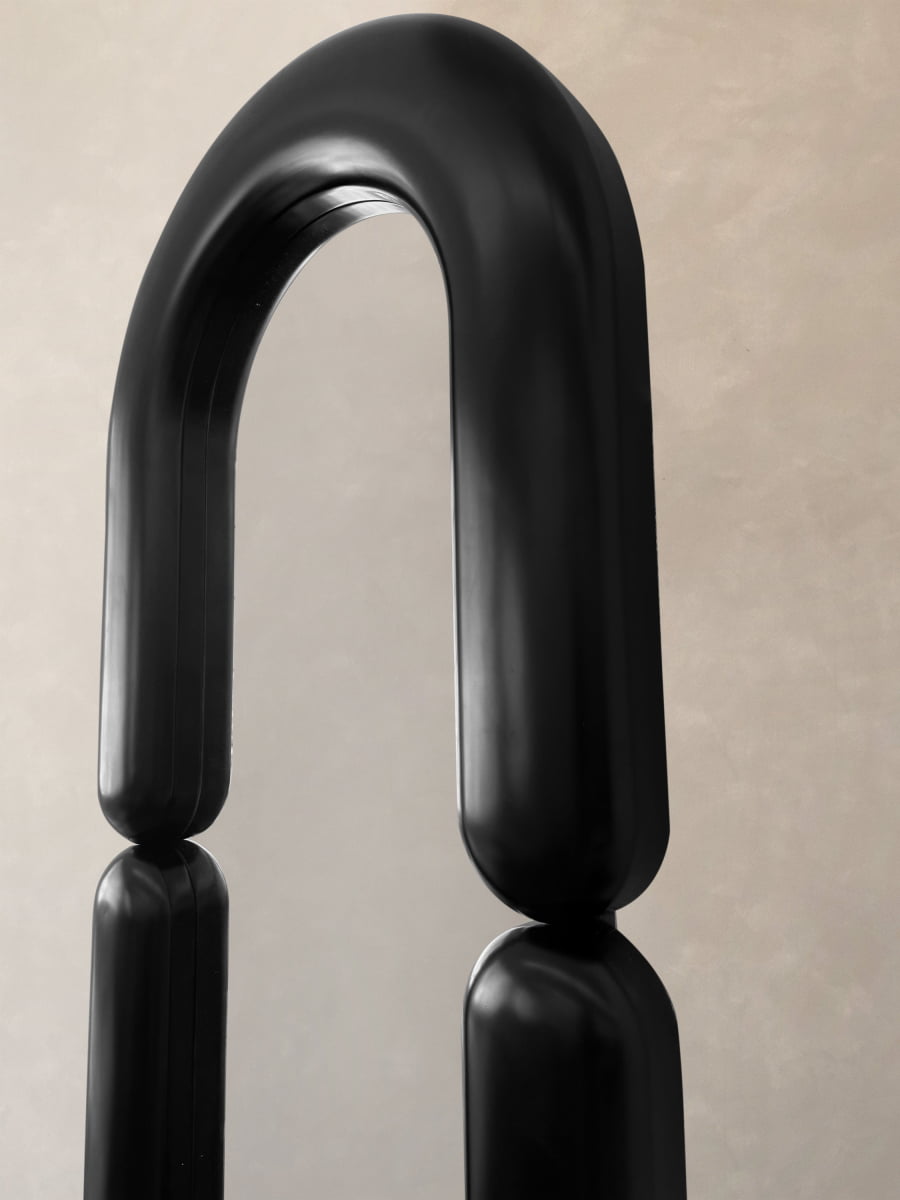 The Pitti Mirror Large in Black features a minimalist, rounded arch design with vertical pillars, creating an artistic statement against a neutral beige background.