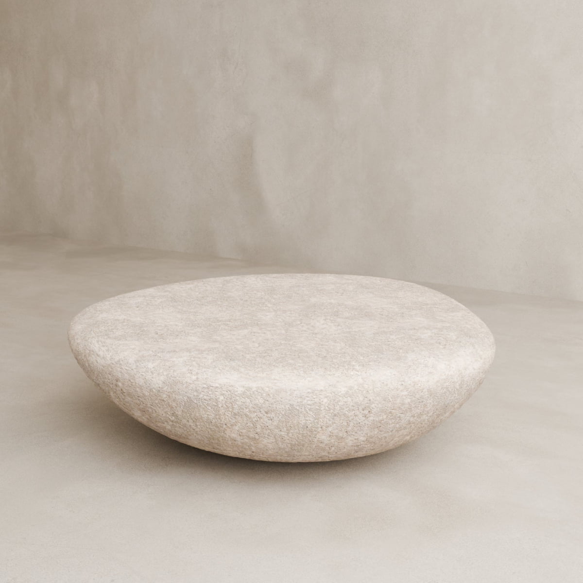 The Pluto Coffee Table features a round, stone-like form with a smooth, slightly domed surface and minimalist design, bringing modern aesthetics to any space against a neutral, textured background.