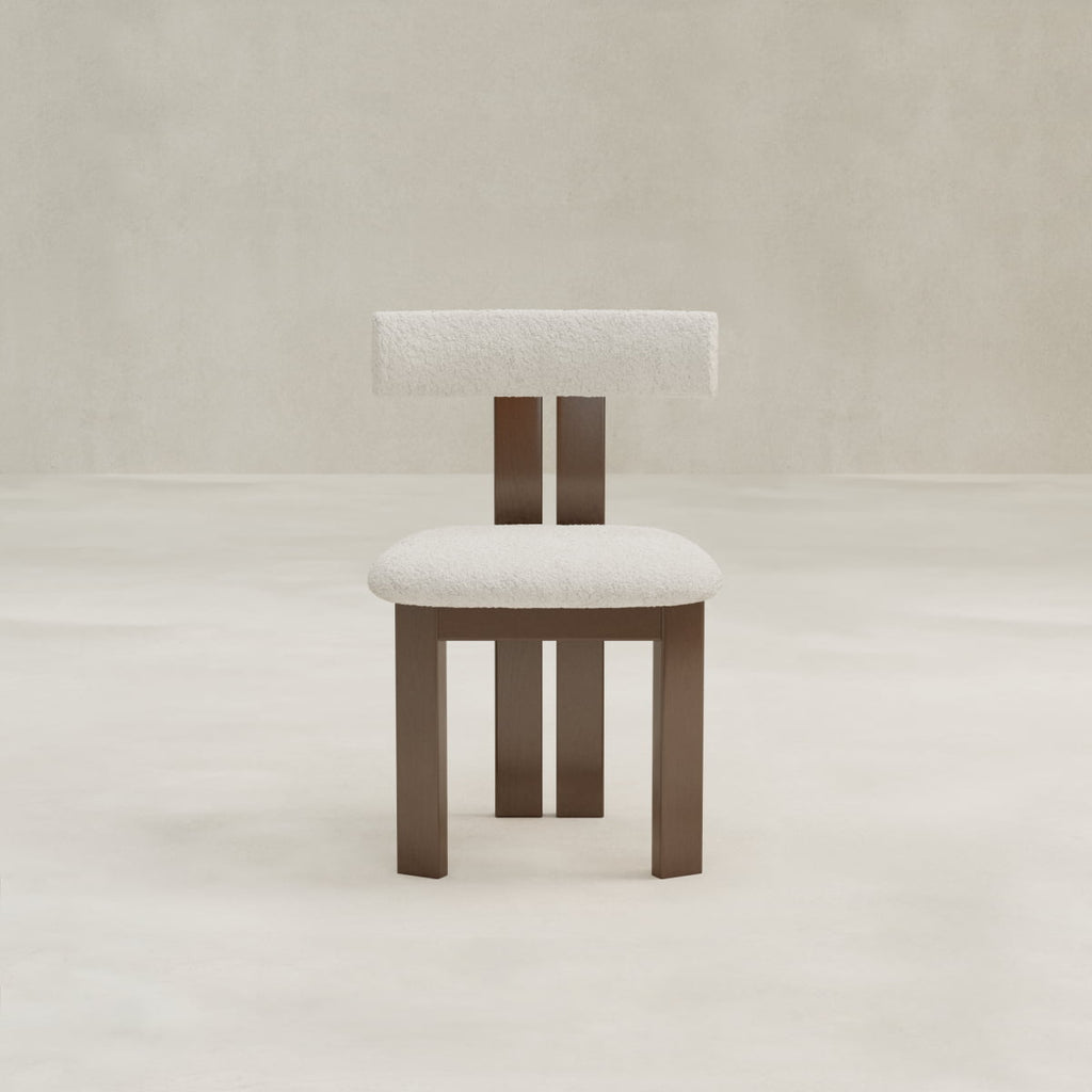 The Radley Dining Chair features a brown wooden frame with square legs, a minimalist design, and padded white bouclé fabric on the seat and rectangular backrest—perfect for adding comfort to any neutral, light-toned room.