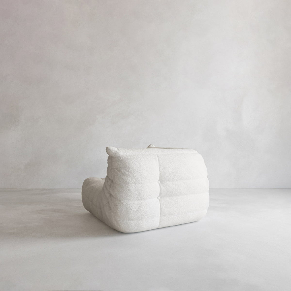 The Rolo Lounge Corner Sofa, in modern white with a textured, quilted surface, adds subtle 70s-inspired style to a minimalistic light gray room with plain walls and floors.