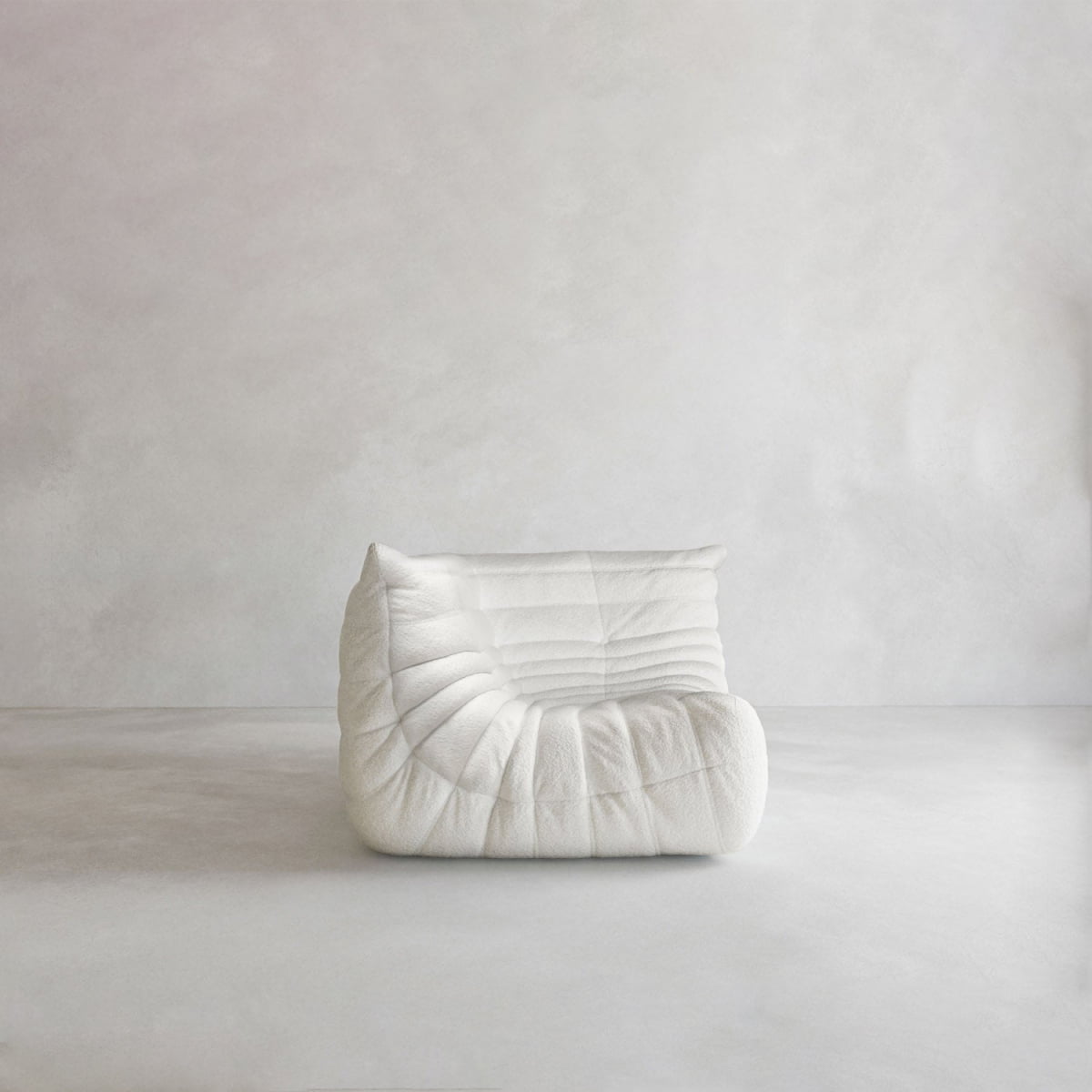 The Rolo Lounge Corner Sofa, a modern low-profile piece with a plush sculpted design, sits in an empty room with light gray walls and floor, creating a minimalist mid-century-inspired aesthetic.