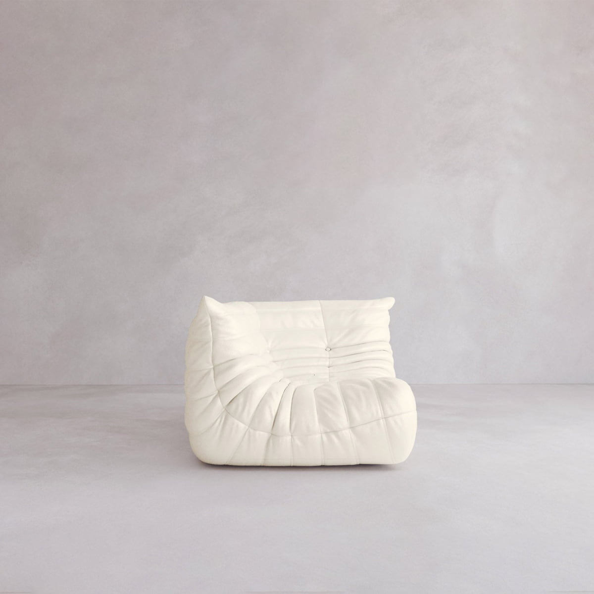 The Rolo Lounge Corner Sofa, a modern white armless piece with soft plush wrinkled design, sits on a light grey minimalistic floor by a matching wall, echoing the subtle mid-century flair of 70s-inspired lounge chairs.
