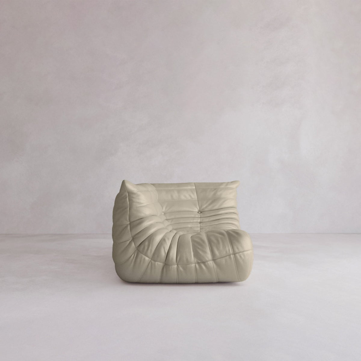 The Rolo Lounge Corner Sofa, a beige, low-profile piece with a 70s-inspired slouchy tufted design, sits alone in a minimalist room with light walls and flooring.