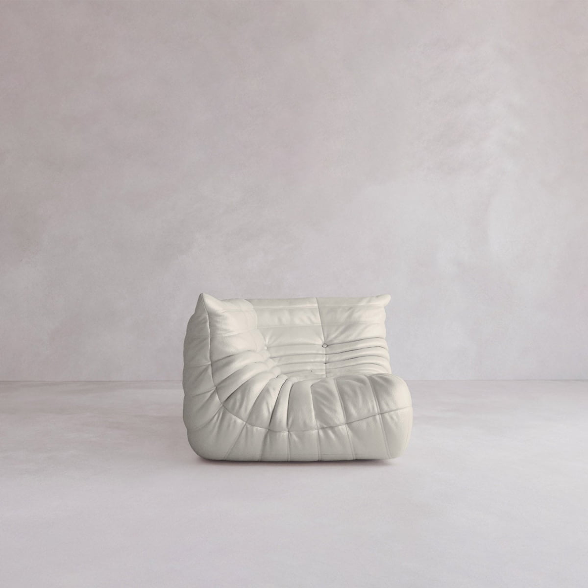 The Rolo Lounge Corner Sofa, a modern armless white piece with soft tufted upholstery and mid-century design, sits alone in a minimalist room with light textured walls and floor.