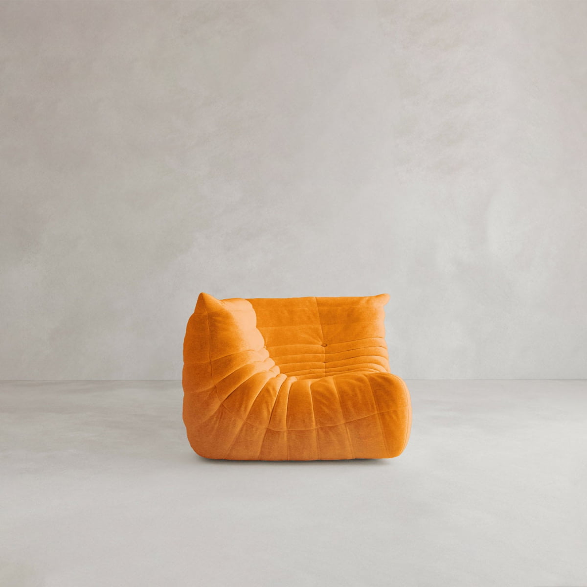 The Rolo Lounge Corner Sofa, a modern low-profile orange piece with plush, tufted cushions and mid-century design influences, sits on a light gray floor against a plain light gray wall.