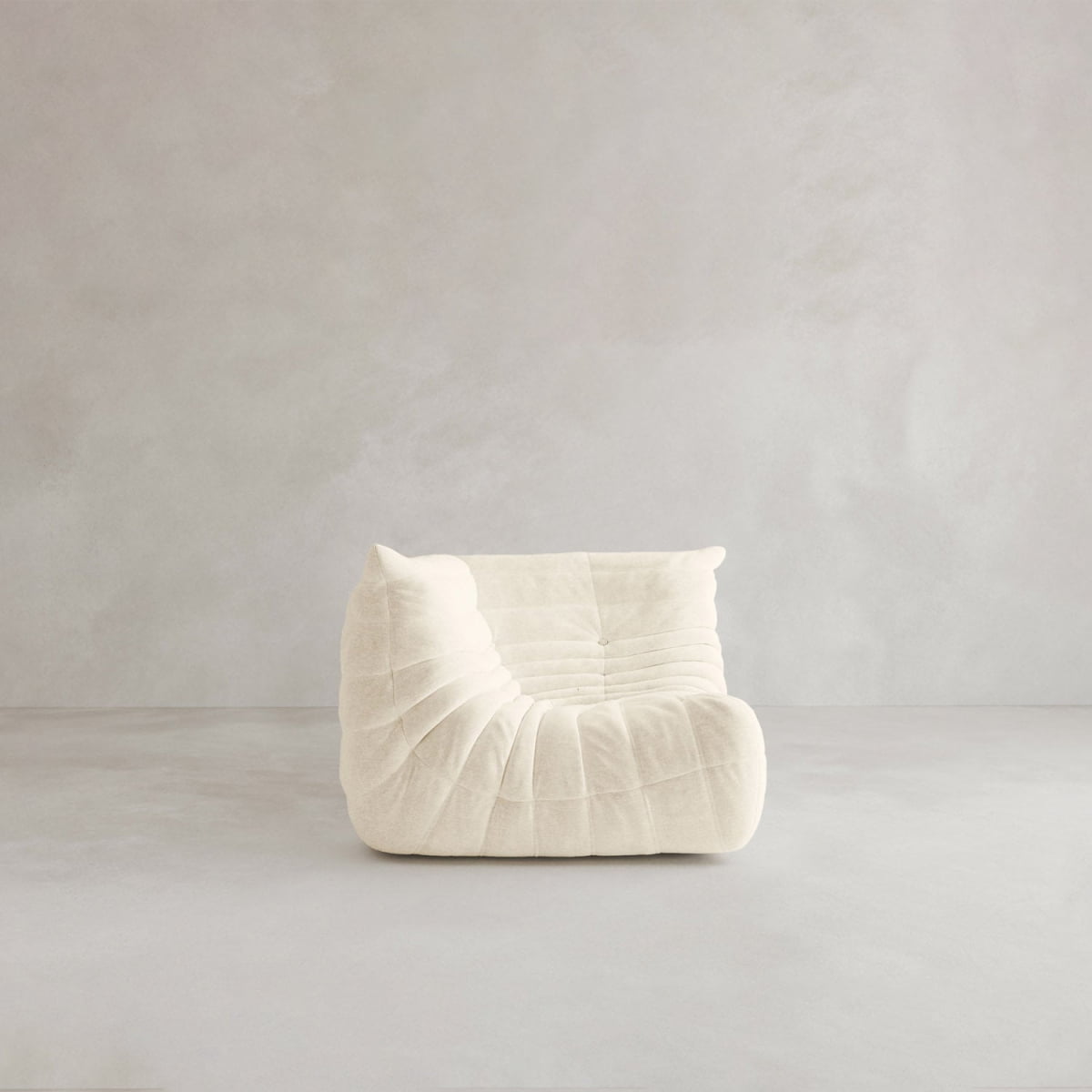 The Rolo Lounge Corner Sofa features modern, armless design and off-white, tufted upholstery, channeling a 70s-inspired vibe as it sits on a light gray floor against a neutral background.