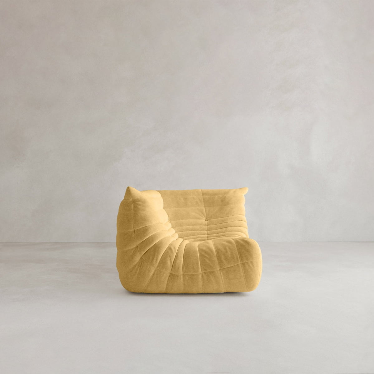 The Rolo Lounge Corner Sofa features a yellow, modern, low-profile silhouette with soft, plush upholstery and a unique ruched design, echoing mid-century style. It sits on a light gray floor against a plain light gray textured wall.