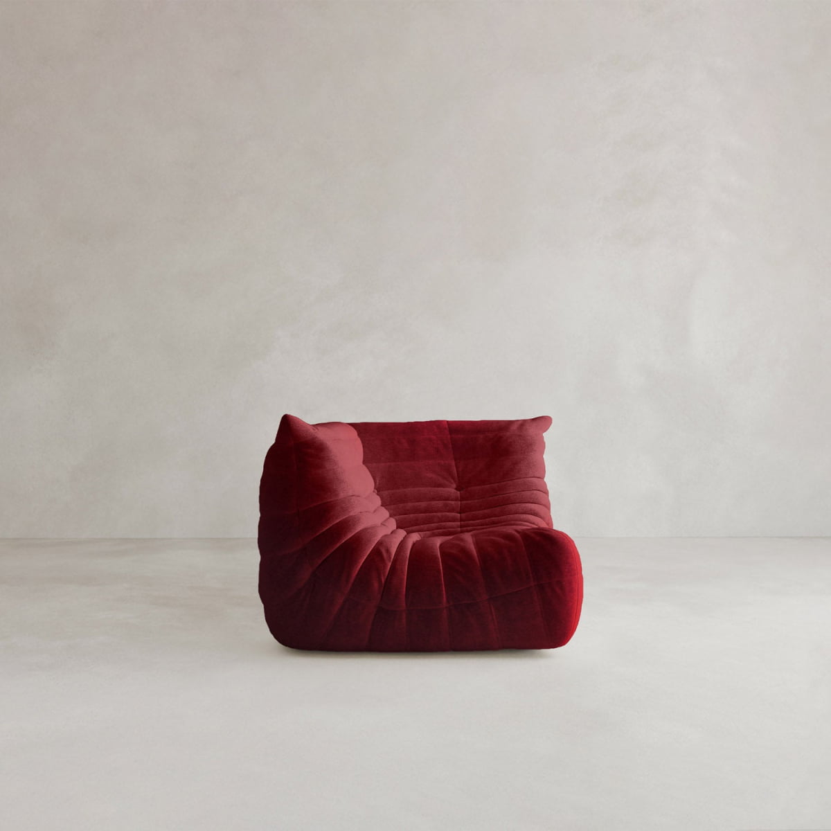 The Rolo Lounge Corner Sofa, a deep red, armless piece with soft quilted texture and mid-century design, sits on a plain light floor against a neutral light grey wall.