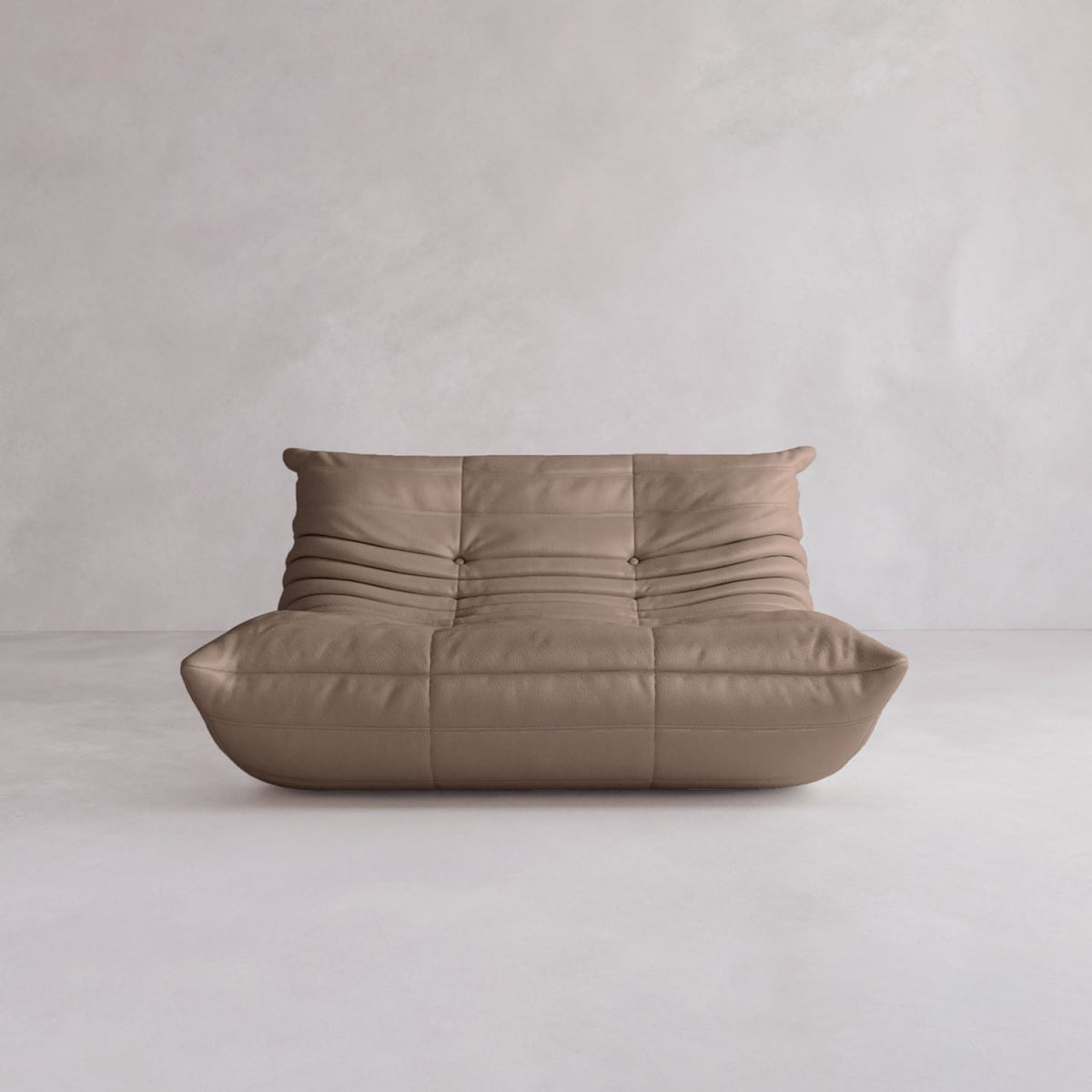 The Rolo Lounge Loveseat, a modern low-profile brown sofa with a tufted cushiony design and subtle modular system, sits against a light gray textured wall and floor.