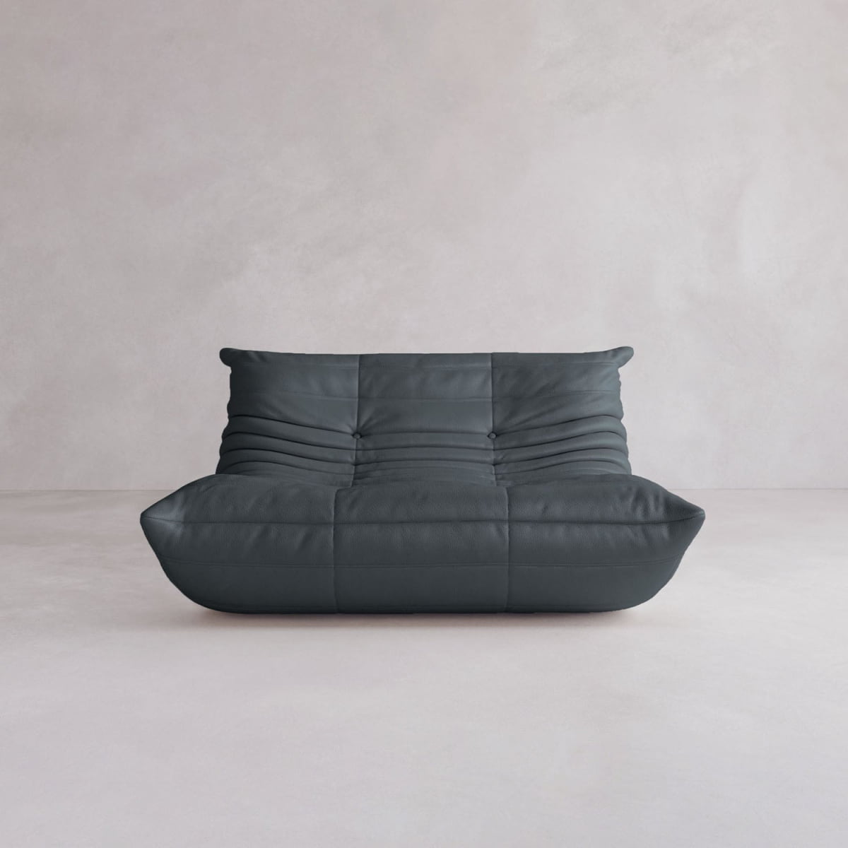 The Rolo Lounge Loveseat is a dark gray, modern, low-profile armless sofa with horizontal stitching and plush, quilted upholstery that channels mid-century design, shown against a plain light gray wall and floor.