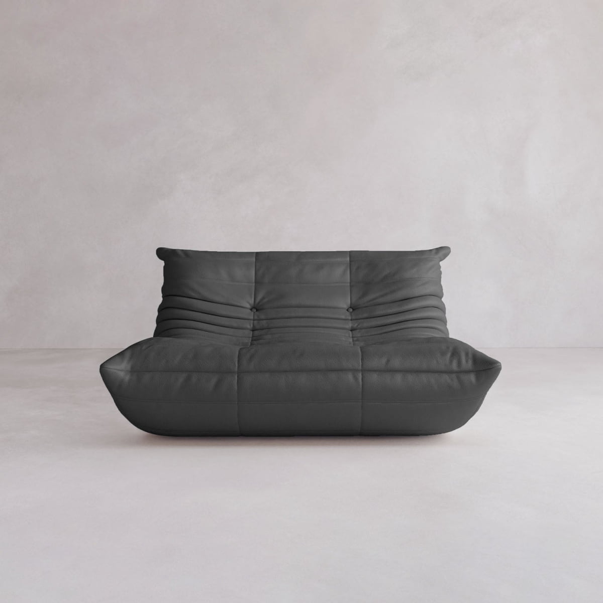 The Rolo Lounge Loveseat, a modern black leather sofa with soft, tufted cushions and mid-century design accents, sits in an empty room with light gray walls and a light floor.