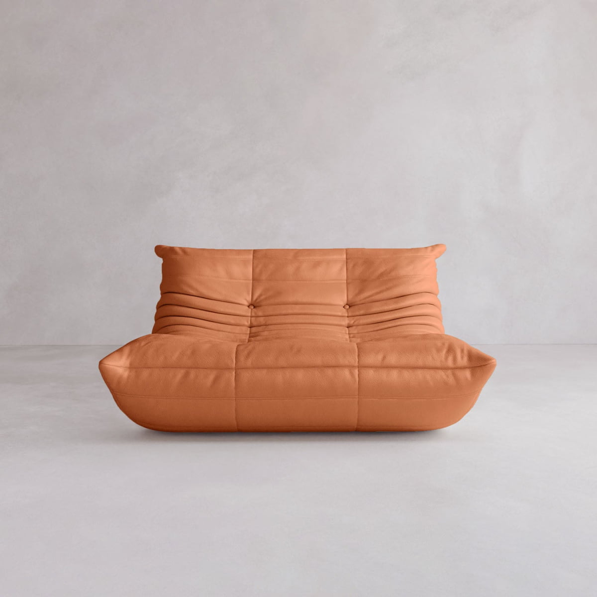 The Rolo Lounge Loveseat is a modern, armless tan leather seat with a low, slouchy silhouette and tufted seams, evoking 70s-inspired style in a minimalist space with light gray walls and flooring.