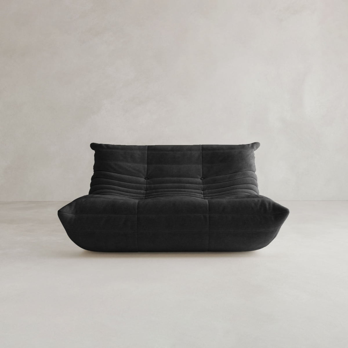 The Rolo Lounge Loveseat, a modern black armless sofa with a low backrest and deep cushioned seat in mid-century style, sits against a light gray minimalist wall and floor.