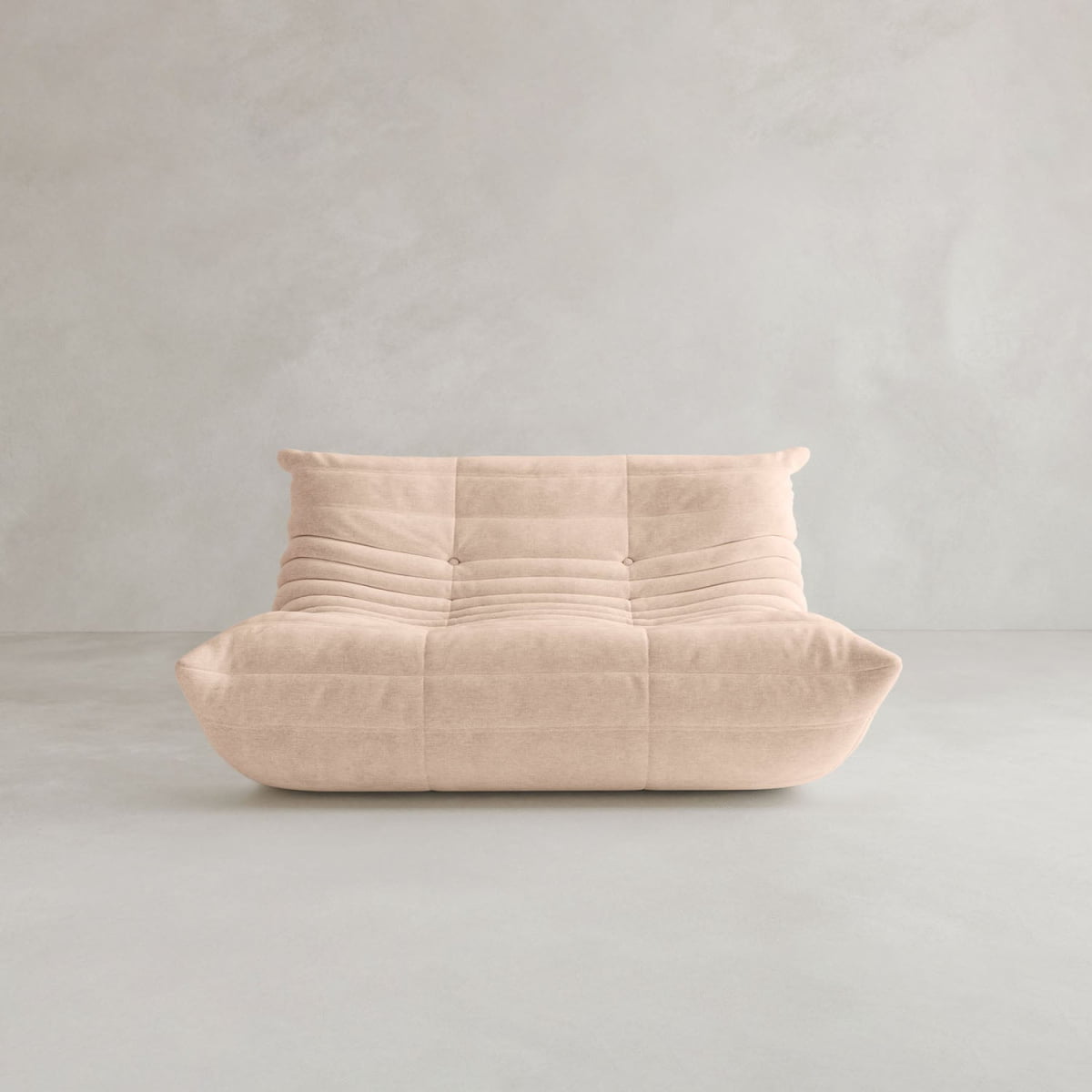 The Rolo Lounge Loveseat is a modern, armless beige sofa with a tufted cushioned design and soft, rounded edges inspired by mid-century style, shown against a plain light gray background.