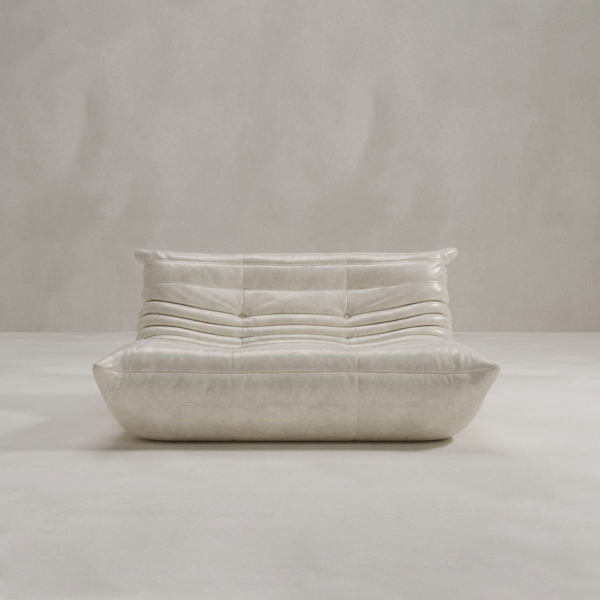 The Rolo Lounge Loveseat, a modern low-profile cream leather sofa with tufted back and seat, stands against a plain light gray wall and floor, radiating mid-century design style.